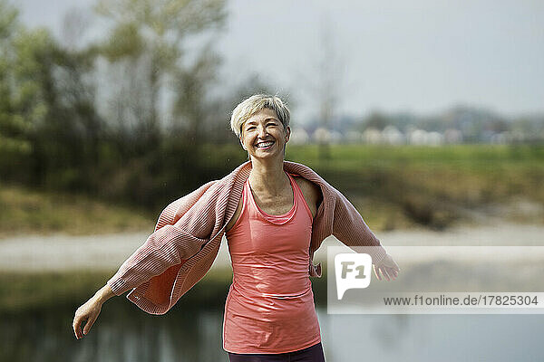 Smiling mature woman standing with arms outstretched on sunny day