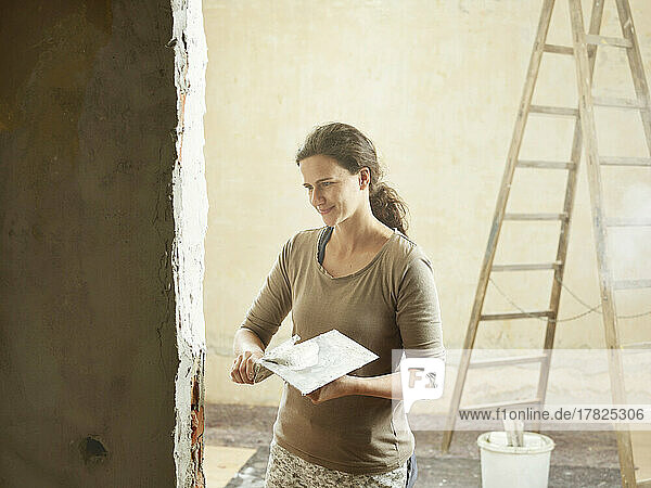Smiling painter plastering wall with spatula in apartment
