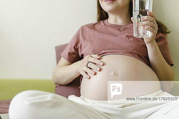 Pregnant woman with glass of water in living room