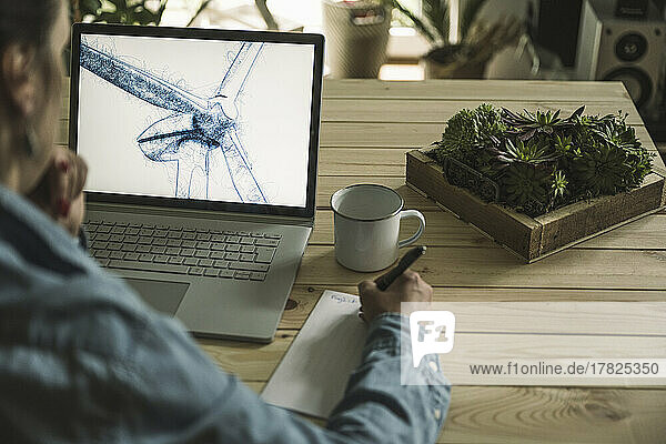 Freelancer writing notes with wind turbine sketch on laptop screen at home