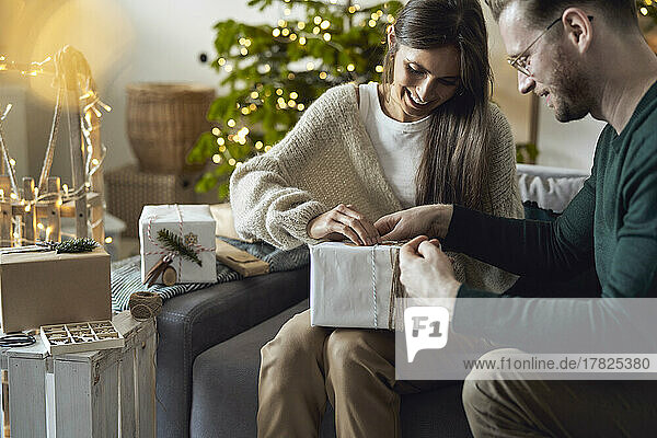 Happy woman with man wrapping Christmas gift at home