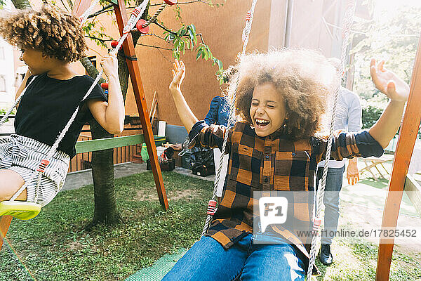 Cheerful boy with sister swinging in backyard