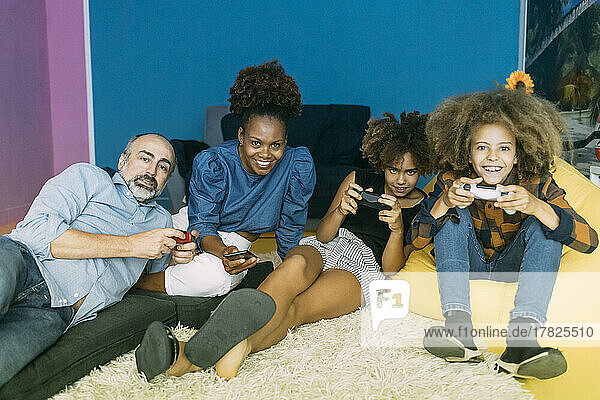 Smiling woman holding mobile phone sitting by man and children playing video game at home