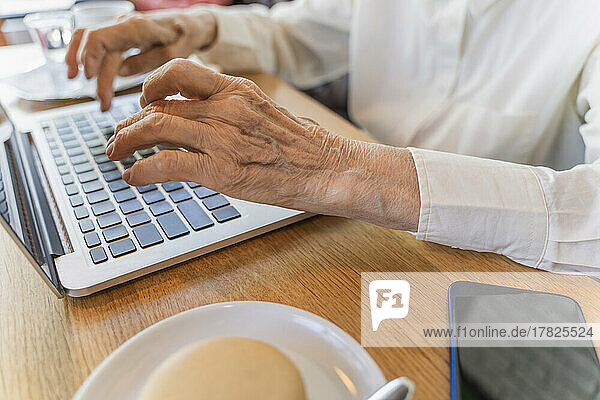 Hände einer älteren Frau  die im Café einen Laptop benutzt
