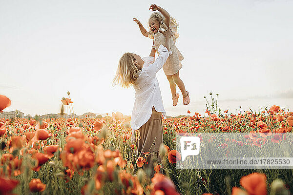 Playful mother lifting daughter in air on sunny day