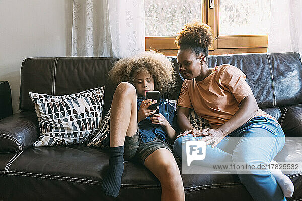 Boy using smart phone sitting with mother on sofa at home