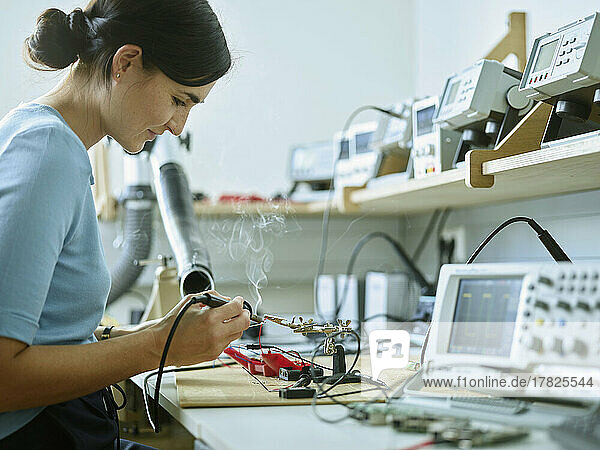 Smiling technician with work tool soldering electronic equipment at desk in laboratory