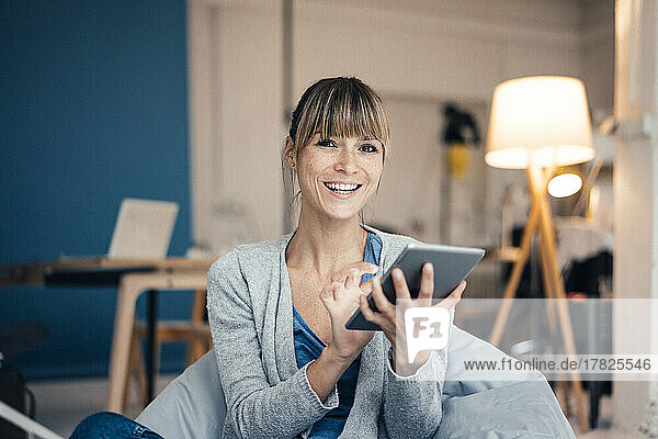 Happy woman sitting on bean bag using tablet PC at home