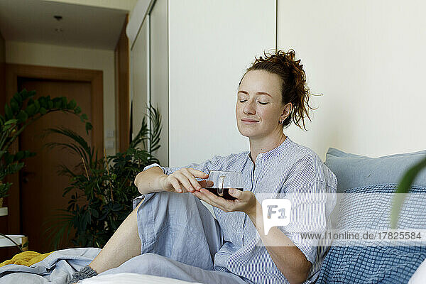 Frau mit geschlossenen Augen sitzt mit einer Tasse Tee zu Hause