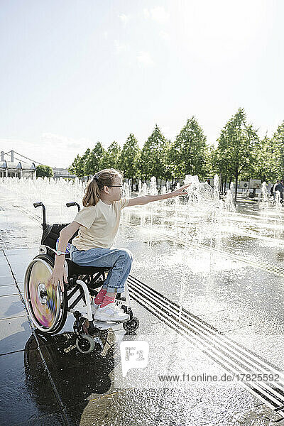 Girl sitting on wheelchair playing with fountain at park
