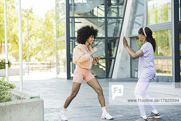 Afro woman doing boxing with mother on footpath