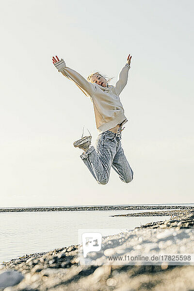Teenager-Mädchen mit erhobenen Armen springt am Strand