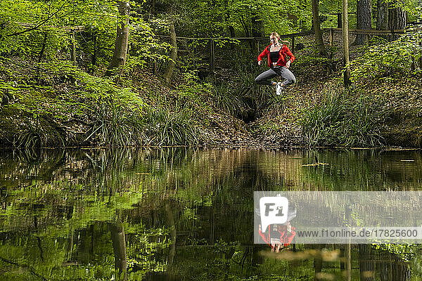 Woman jumping over lake in forest