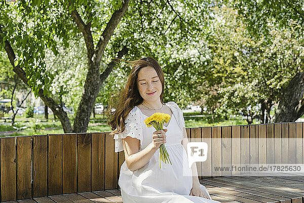 Pregnant woman with flowers sitting in public park