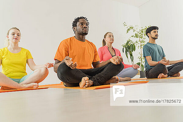 Men and women practicing lotus position yoga meditating at health studio