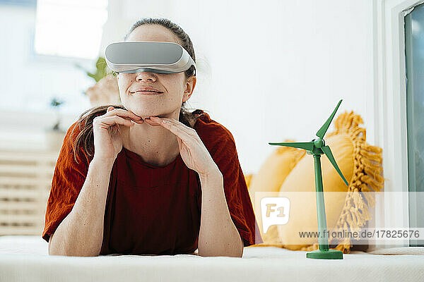 Lächelnde Frau mit VR-Brille und Windturbinenmodell  die zu Hause liegt