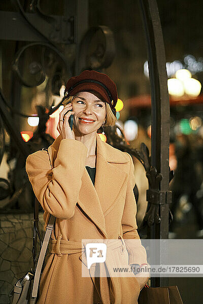 Smiling woman wearing hat talking on phone at night