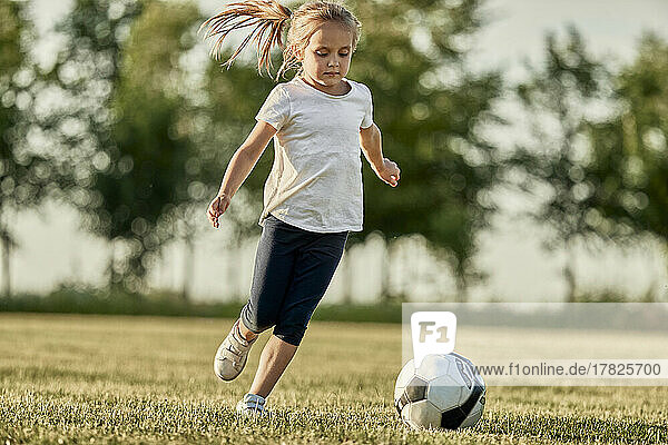 Blond girl playing soccer at sports field on sunny day