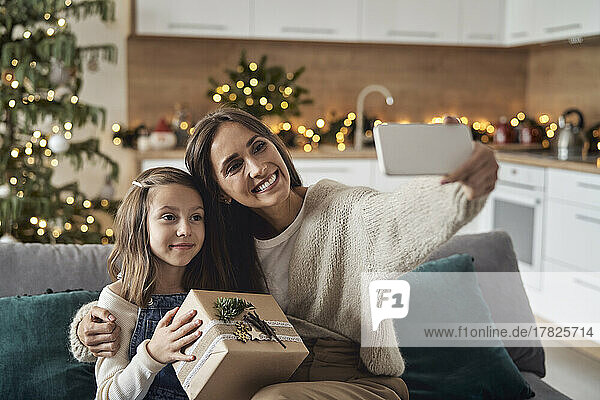 Happy woman taking selfie with daughter through smart phone at home