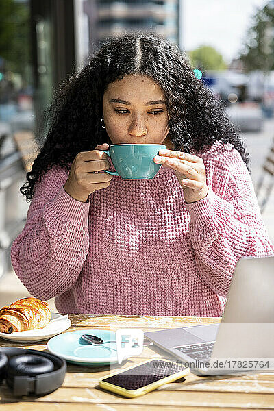 Young woman drinking coffee sitting at sidewalk cafe