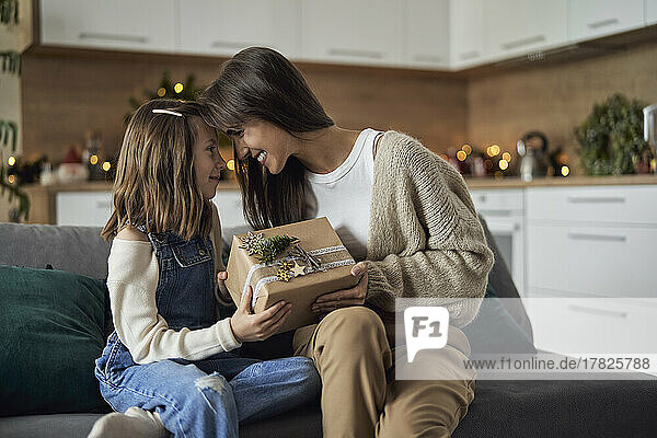 Smiling woman and daughter sharing Christmas gift with each other at home