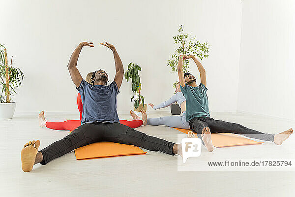 Gemischtrassige Paare üben gemeinsam Dehnübungen im Yoga-Studio
