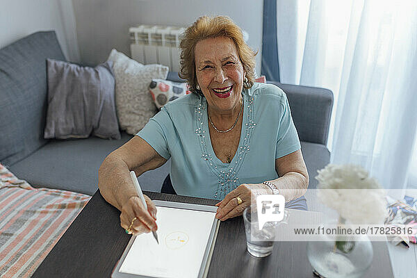 Happy senior woman with tablet PC sitting at table