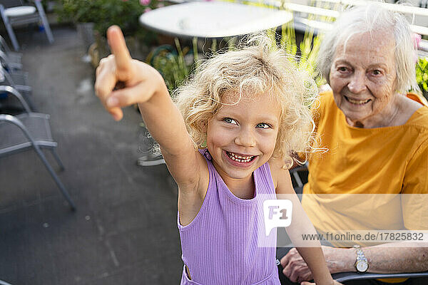 Glückliche Seniorin blickt auf ihre Enkelin und zeigt auf den Balkon