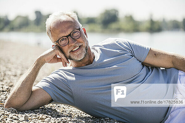 Smiling man lying at riverbank on sunny day