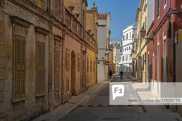 Blick auf ein Paar  das eine pastellfarbene Straße im historischen Zentrum entlanggeht  Ciutadella  Menorca  Balearen  Spanien  Mittelmeer  Europa