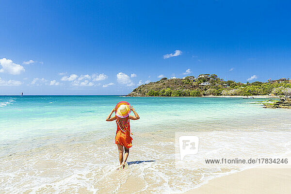 Schöne Frau mit orangefarbenem Kleid und Strohhut an einem tropischen Strand  Antigua  Westindien  Karibik  Mittelamerika