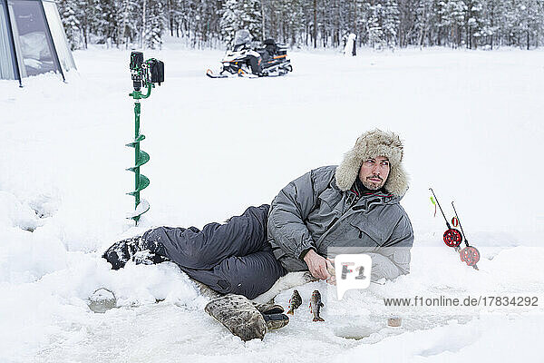 Man lying on ice while fishing from a hole  Lapland  Sweden  Scandinavia  Europe