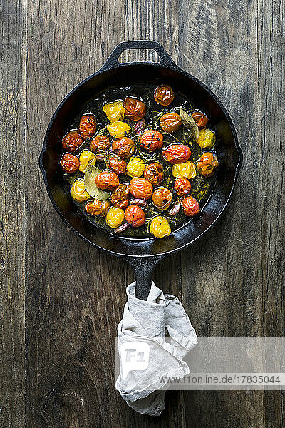 Bunte  geröstete Tomaten in einer Pfanne mit Kräutern und Knoblauchzehen