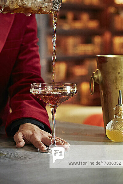 A cocktail being poured into a martini glass