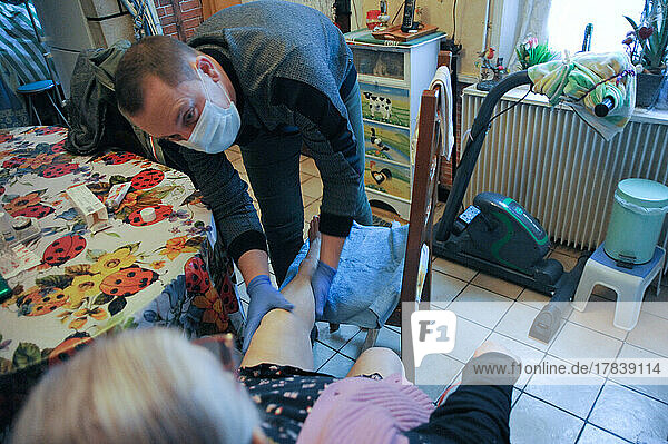 Liberal nurse performs at the home of an 86-year-old patient a leg massage and the installation of compression stockings.