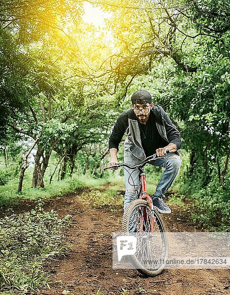 A guy riding a bike in the countryside  Person riding a bike in the countryside  Portrait of a guy in cap riding a bike on a country road  Bicyclist person on his bike on a country road forest