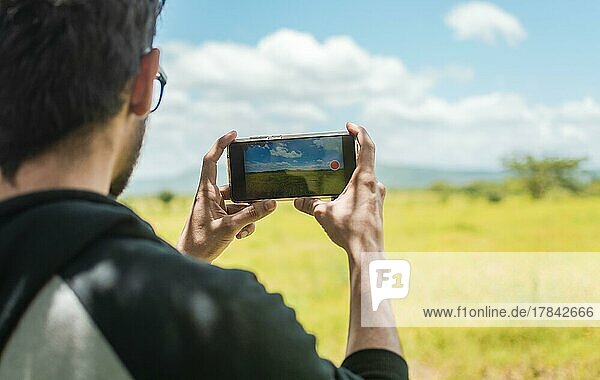 Rückansicht einer Person  die ein Feld mit ihrem Mobiltelefon fotografiert  Rückansicht eines Mannes  der ein Feld fotografiert  Nahaufnahme eines Touristen  der eine Landschaft fotografiert