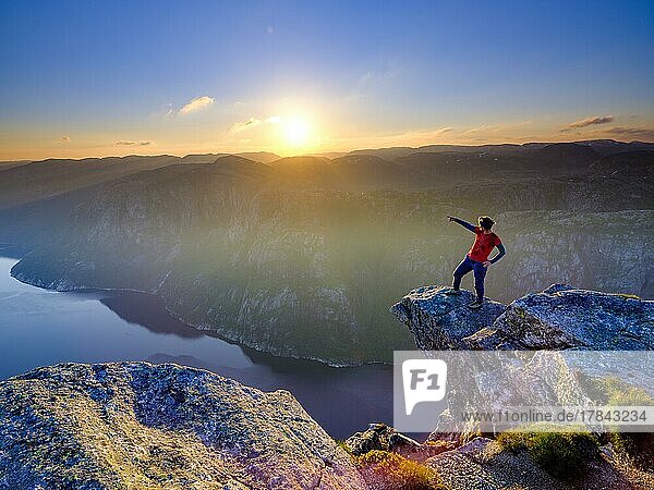 Woman standing on a rocky outcrop at Kjerag above the Lysefjord pointing her finger into the distance  sunset  Lyseboten  Rogaland  Norway  Europe
