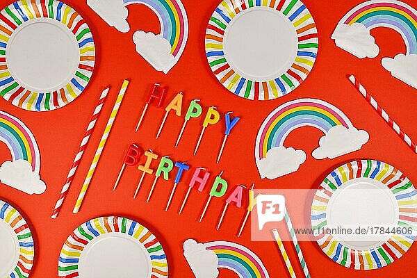 Geburtstagsparty flach legen mit bunten Tellern Regenbogen Servietten Kerzen und Trinkhalme auf rotem Hintergrund