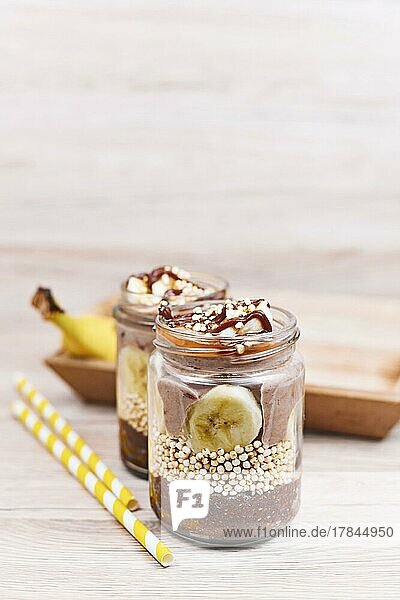 Gesundes Schichtdessert mit Bananenfruchtscheiben  gepufftem Quinoa Korn und Schokoladen Chiasamenpudding im Glas