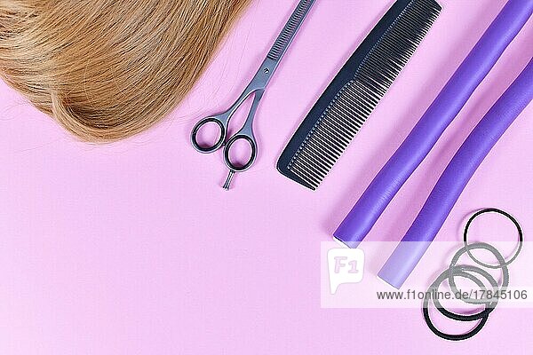 Hair Styling Konzept mit dunkelblondes Haar  elastische Haarbänder  Kamm  Ausdünnung Schere  und Papillote Lockenwickler auf rosa Hintergrund mit Kopie Raum