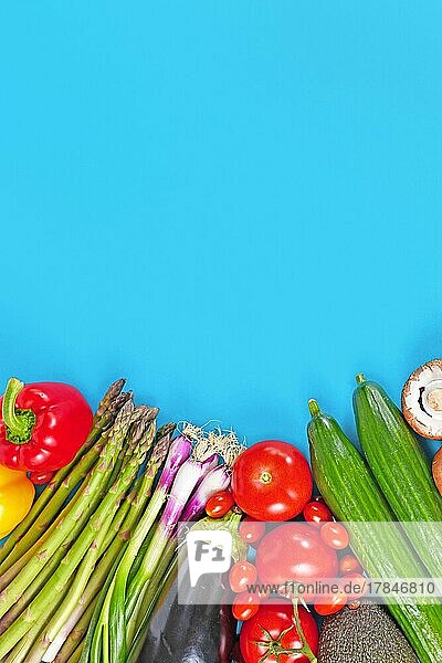 Raw vegetables including tomatoes  bell pepper  spring onions  eggplant  asparagus  cucumber and avocado on blue background with copy space