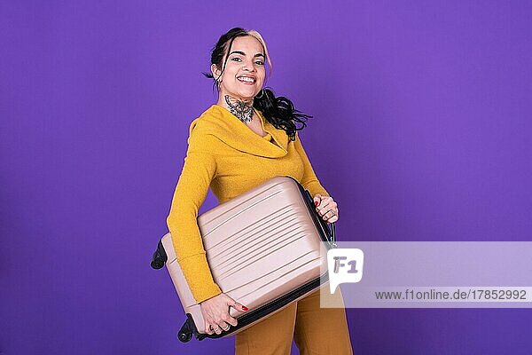 Attraktive glückliche Frau Reisende hält ihren Koffer gegen lila Hintergrund