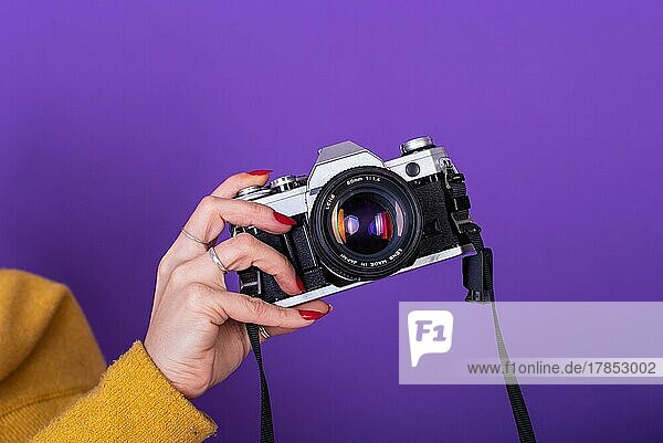 Nahaufnahme einer weiblichen Hand  die eine Filmkamera vor einem violetten Hintergrund hält