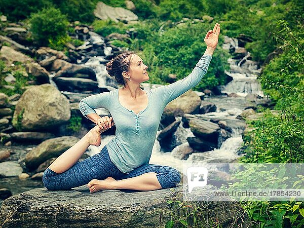 Vintage Retro-Effekt Hipster-Stil Bild der sportlich fit Frau tun Yoga-Asana Eka pada rajakapotasana  einbeinigen König Taube Pose an tropischen Wasserfall. Himachal Pradesh  Indien  Asien
