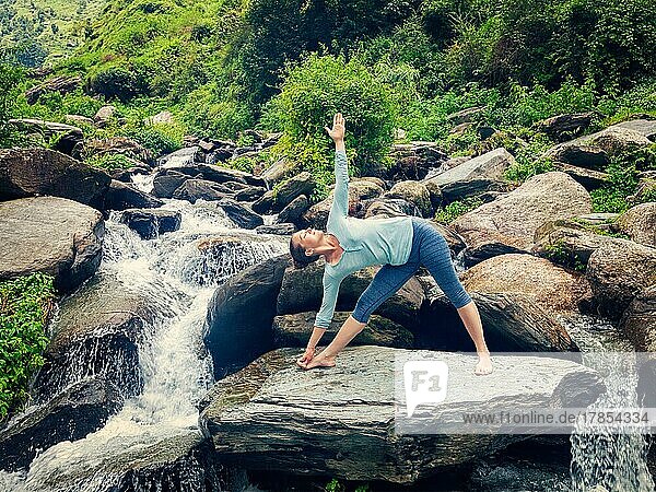 Vintage Retro-Effekt Hipster-Stil Bild der Frau tun Ashtanga Vinyasa Yoga Asana Utthita trikonasana  erweiterte Dreieckspose im Freien an einem Wasserfall im Himalaya