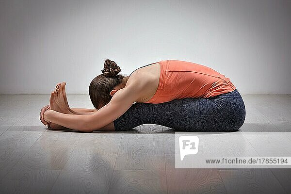 Sportlich fitte Frau übt Ashtanga Vinyasa Yoga Rückenbeuge Asana Paschimottanasana  sitzende Vorwärtsbeuge