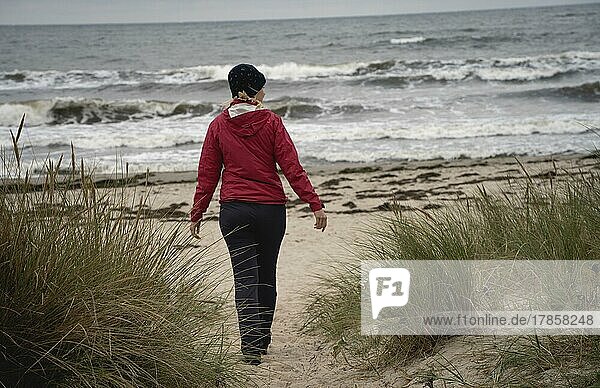 Frau in rot läuft an Sandstrand an der Ostsee bei düsterem Wetter  Insel Rügen  Deutschland  Europa