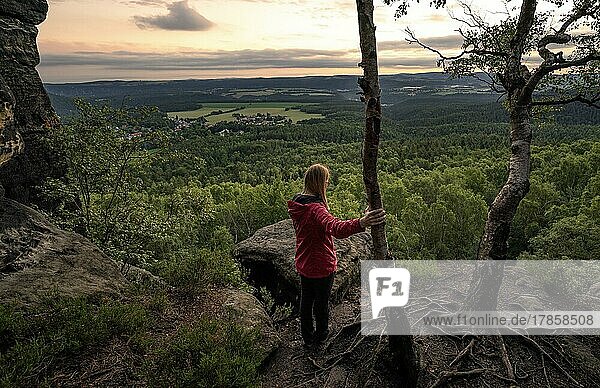 Frau in rot steht auf der Spitze einer Gebirgskette im Elbsandsteingebirge und beobachtet den Sonnenaufgang  Elbsandsteingebirge  Dresden  Deutschland  Europa