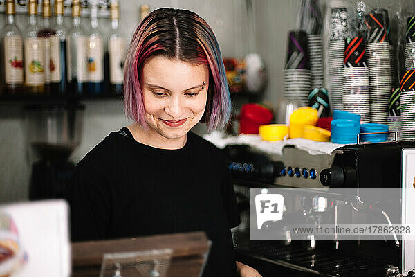 Happy young female barista standing at checkout counter in coffee shop